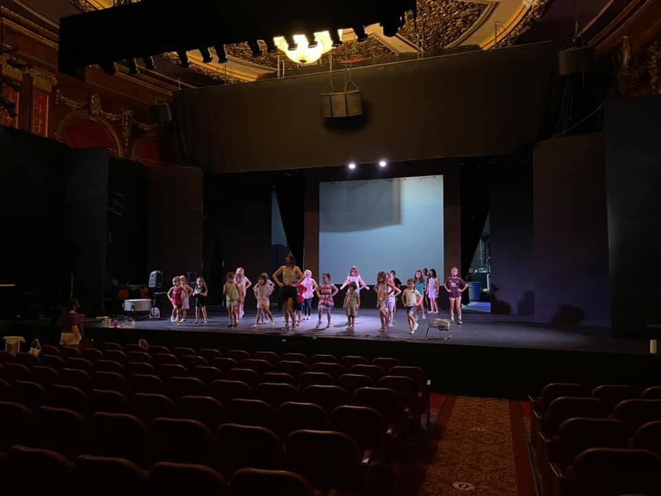 A group of children on a stage practicing in an empty theatre