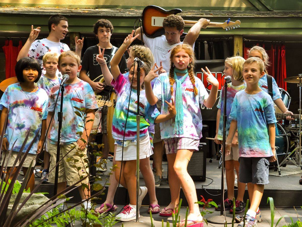 Several children in tie-die shirts on stage with musical instruments
