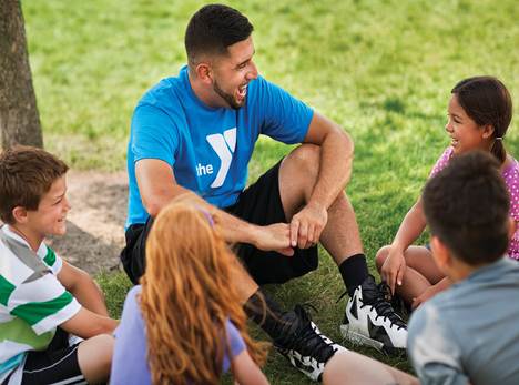 A YMCA counselor with four students sitting in the grass